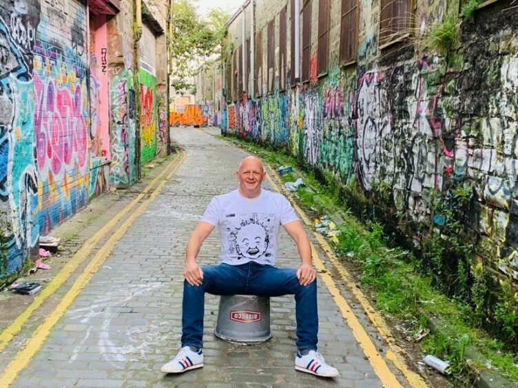 street poet Gary Robertson sitting on an upturned bucket in an alley in Dundee.