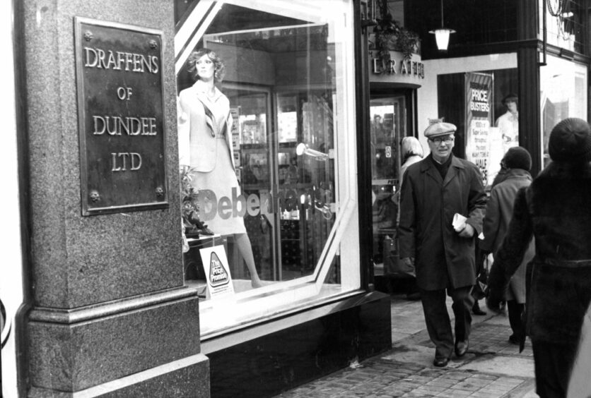 Black and white photo shows a man walking past a shop window and a brass sign for Draffens of Dundee Ltd in 1981.