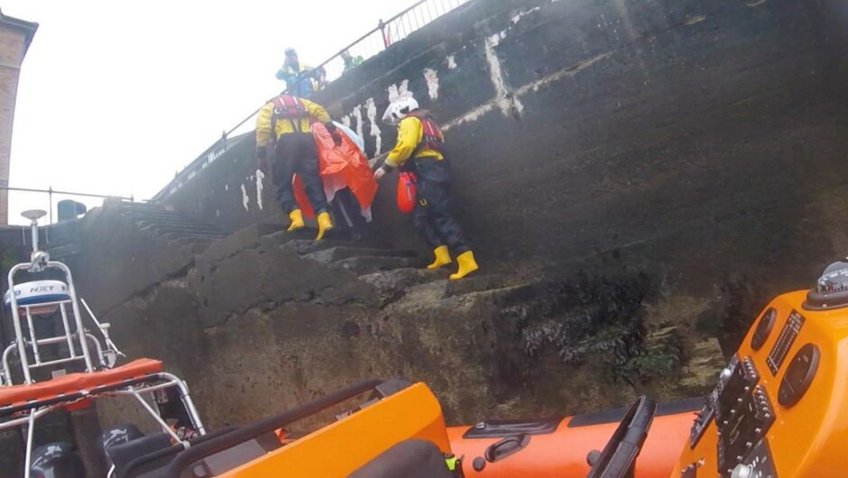 A woman being led up the steps of a harbour after being rescued by Kinghorn RNLI