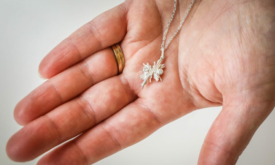 Elizabeth Humble holding a silver necklace made of fine lines and two diamonds in her hand.