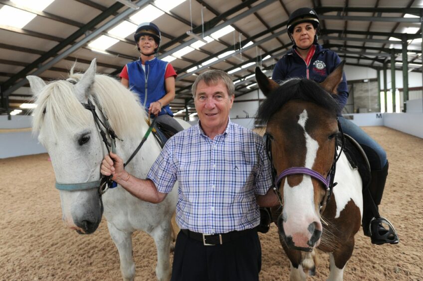 Geoff Brown in indoor riding arena holding two ponies by their bridles
