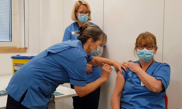 Lynda Smyth receiving the first vaccine from Marion McLaggan with fellow Covid vaccinator Gill Allan.