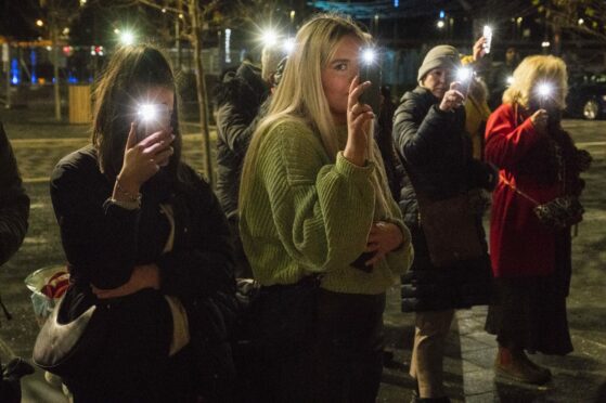 People at the vigil shine their phone lights as the names of the women were read out.