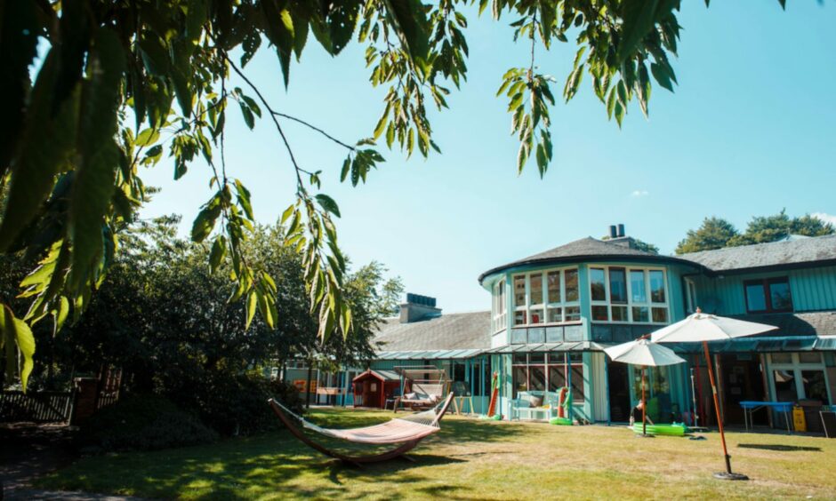 Rachel House exterior, a warm bluey green building with large windows and extensive gardens