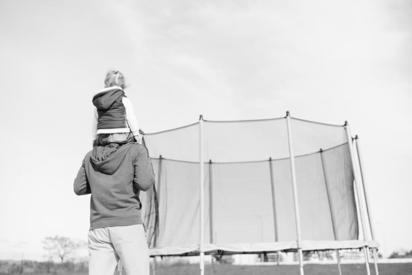 Man carries child on shoulders towards trampoline.