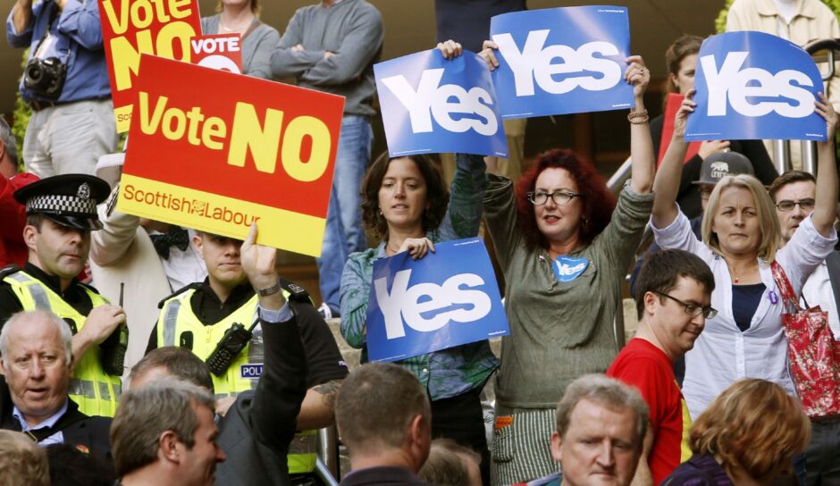 photo shows a crowd of people, some holding Vote No placards, the others Yes placards.