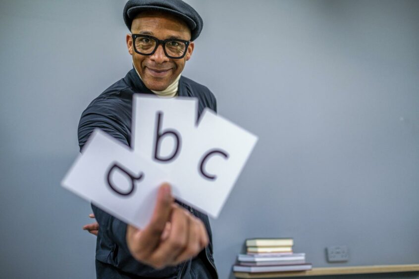 Jay Blades holding up cards with the letters a, b and c.
