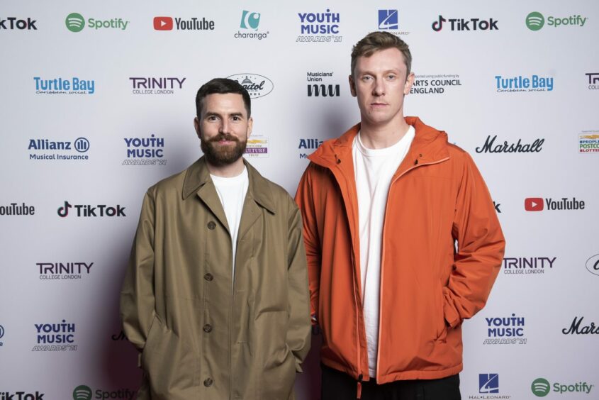 Music duo Bicep in front of a sponsors board.