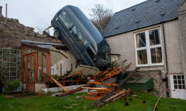 Front-on view of van that has driven through wall and landed on greenhouse in Johnshaven back garden.