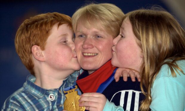 British curling skip Rhona Martin, displaying her Olympic gold gold medal, is kissed by son Andrew Martin, six, and daughter Jennifer Martin, nine, at the Greenacres Curling Club in Howwood, February 26, 2002