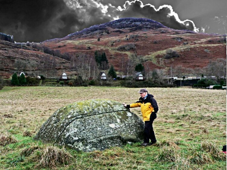 David Cowan standing next to a big rock in a field with foreboding clouds behind.
