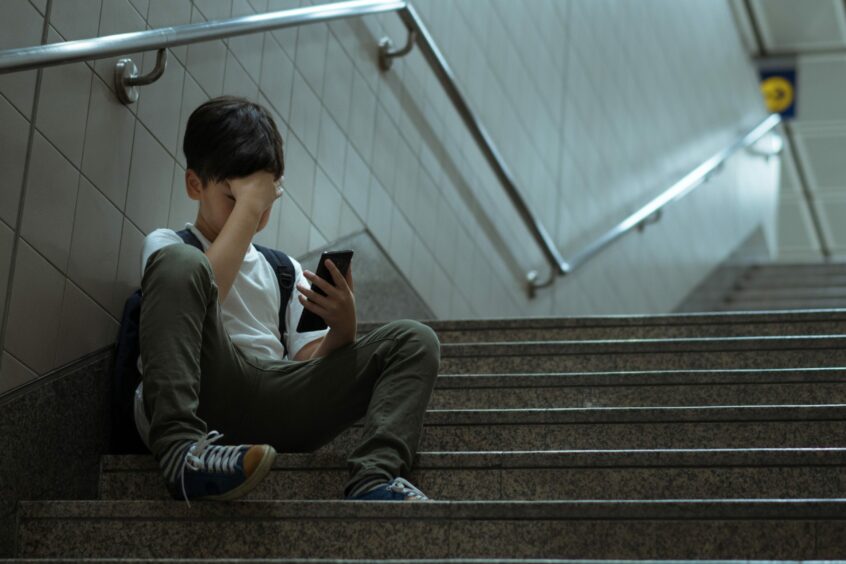 A boy sitting on stairs with his head in his hand looking at a phone