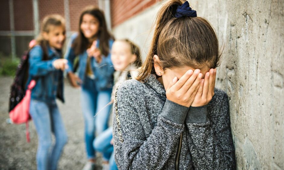 A girl with her head in her hands as she is teased and bullied by other girls
