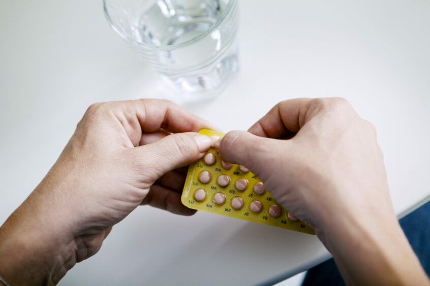 Photo shows a woman taking a Hormone Replacement Therapy tablet out of a blister pack.