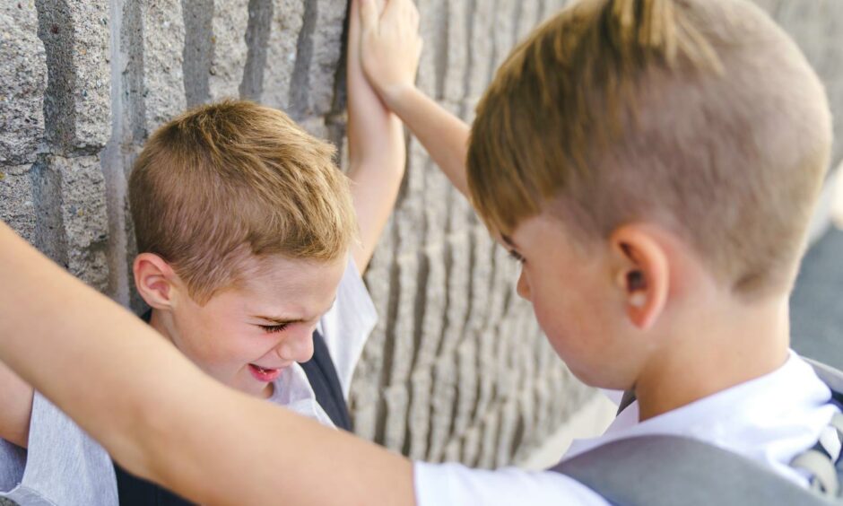 A boy pinning another boy's arms to a wall