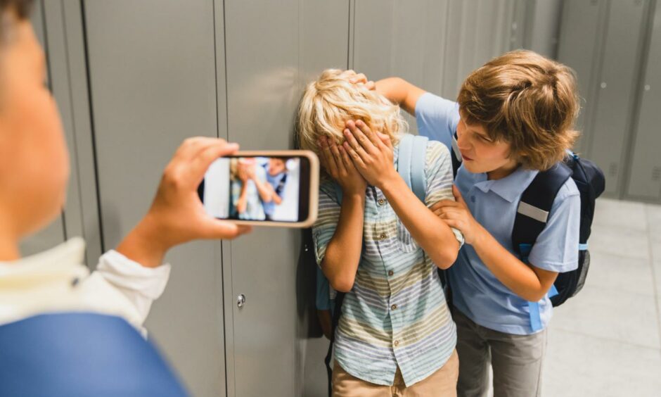 A boy being bullied as another boy films it on his phone