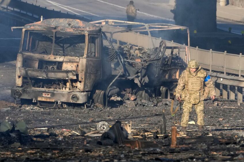 Ukrainian soldier walks past debris of a burning military truck, on a street in Kyiv, Ukraine