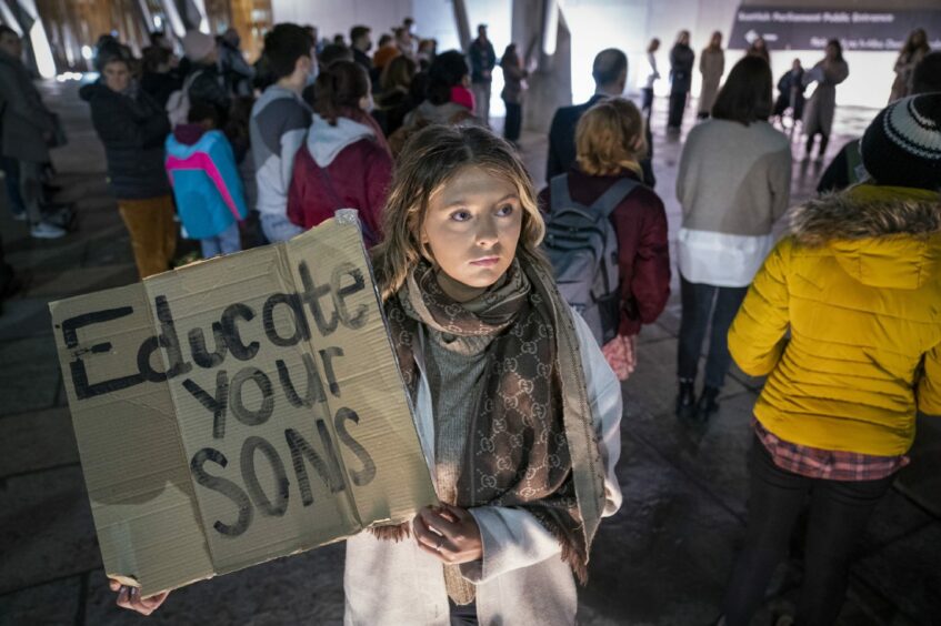 woman holding a cardboard sign which reads 'Educate your sons'.