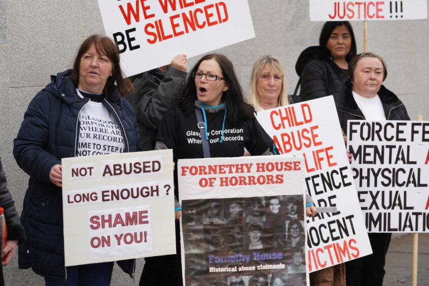 photo shows a group of women carrying placards with messages such as 'Not abused long enough? Shame on you' and 'Fornethy House of Horrors'