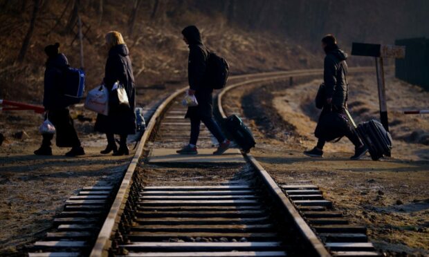 A family from Ukraine walk over a railway line with their luggage after crossing a border point into Poland at Kroscienko, in the south east of the country