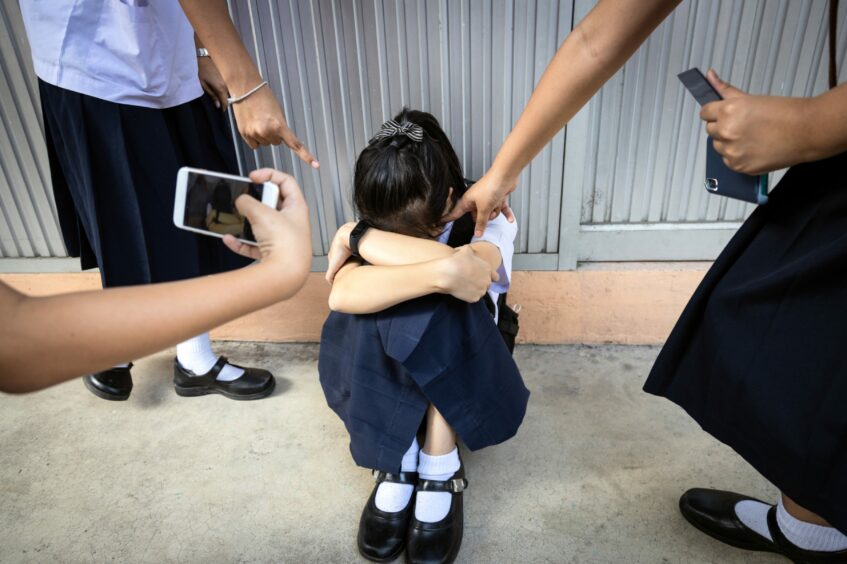 A girl being bullied by fellow school pupils who are filming it