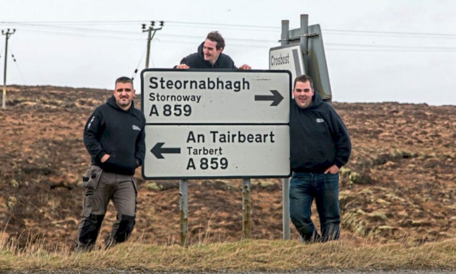 Peat & Deisel band members standing next to road signs for Stornoway and Tarbert