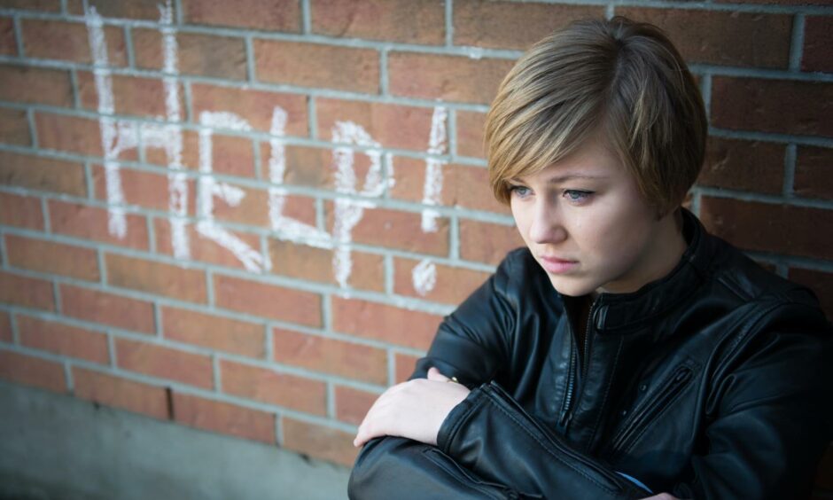 A child sitting near a wall with the word 'help' written on it