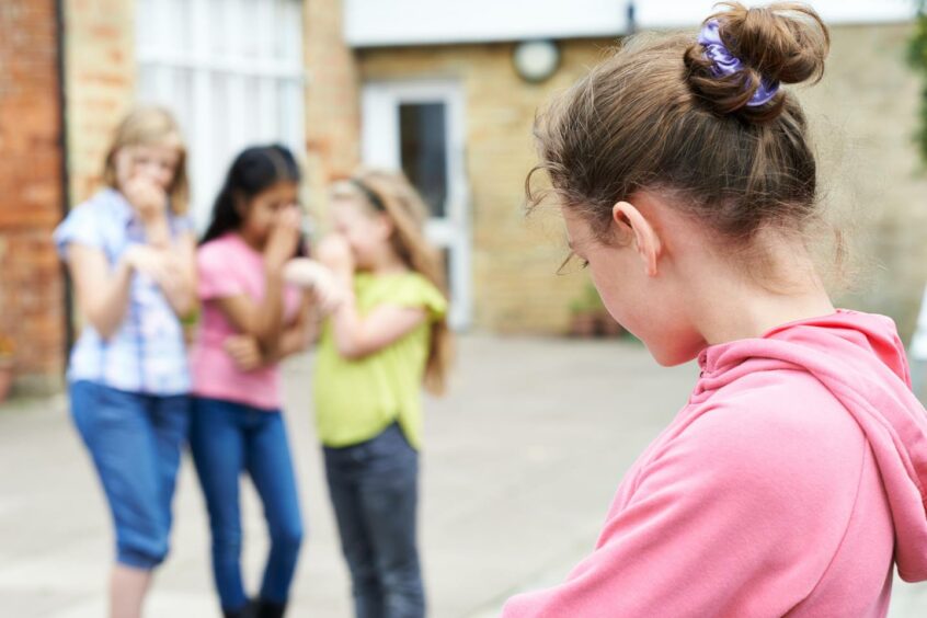 a girl in the school playground with 3 other girls looking and laughing at her