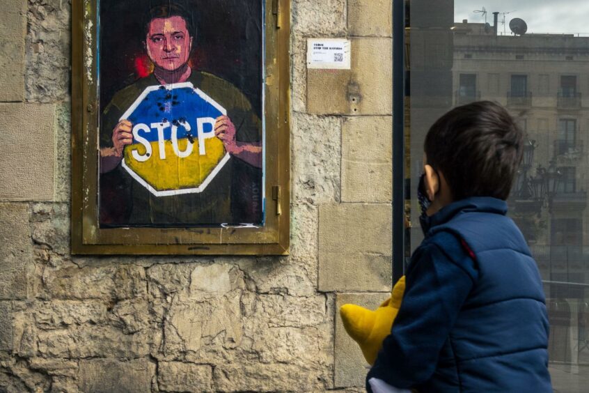 Children look at painting on Zelensky with a sign to stop the war following Russia's invasion