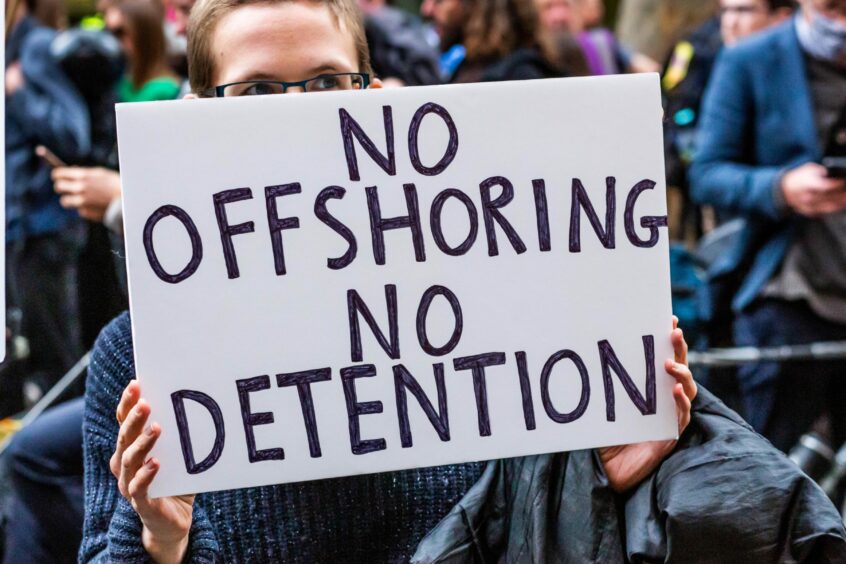 protesrer hold sign saying 'No offshoring, no detention'