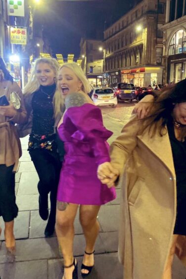 Lynne Hoggan in party dress running along a pavement with friends
