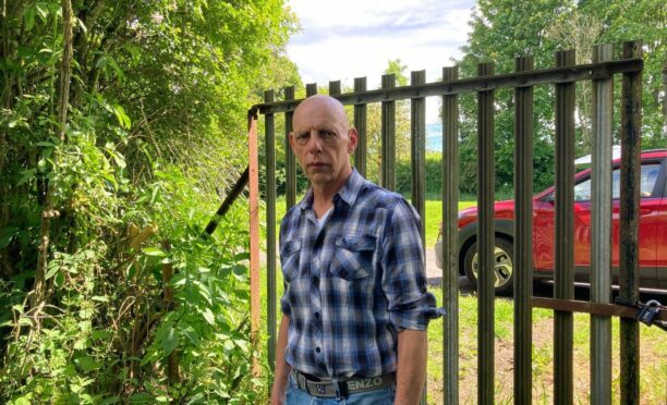 Balhomie Wood campaigner Michael Foreman at a metal gate surrounded by trees.