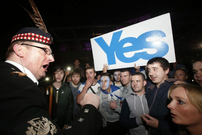group of young man holding a Yes banner watching a man in Highland dress.