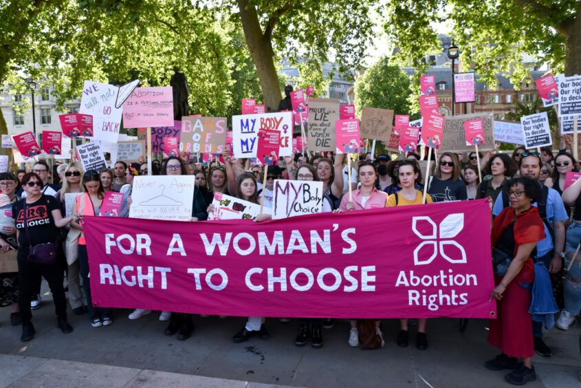 large crowd of women with placards behind a banner which reads 'For a woman's right to choose'
