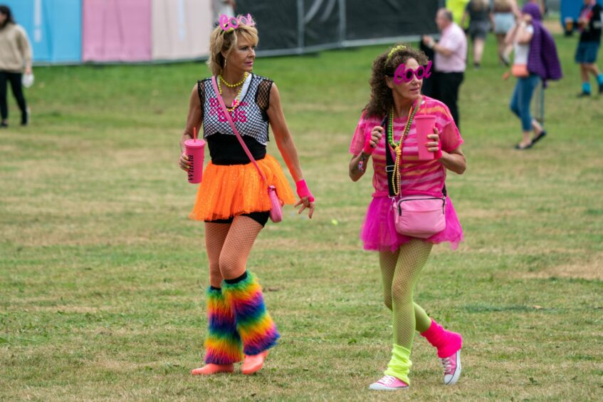 Two women dressed in 80s fashions walking across the Rewind Scotland showground.