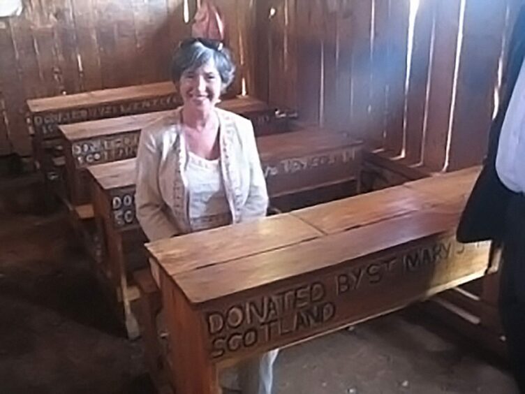 Sheila Mcluckie sits at a desk inscribed with the words 'donated by St Mary's Primary School, Scotland'