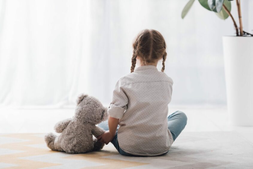 rear view of little child sitting on floor with her teddy bear toy; 