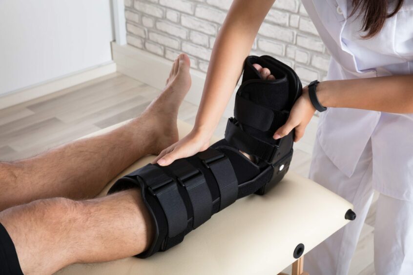 A Close-up Of A Orthopedist Putting Walking Brace To Patient's Leg