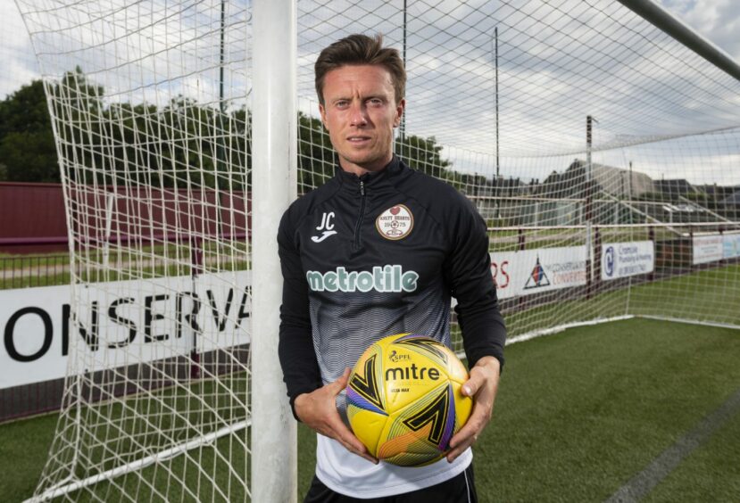 Joe Cardle leans against a goalpost holding a ball at Kelty Hearts' ground.