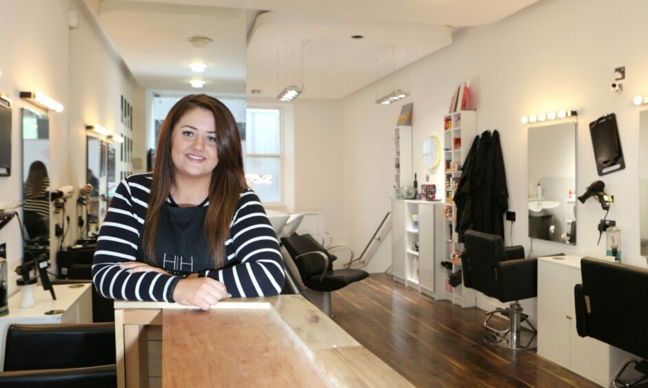 Emma, a woman with long brown hair and a stripy shirt standing in her beauty salon.