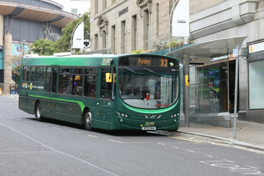 A green bus going to Fintry stopped at a bus stop. 