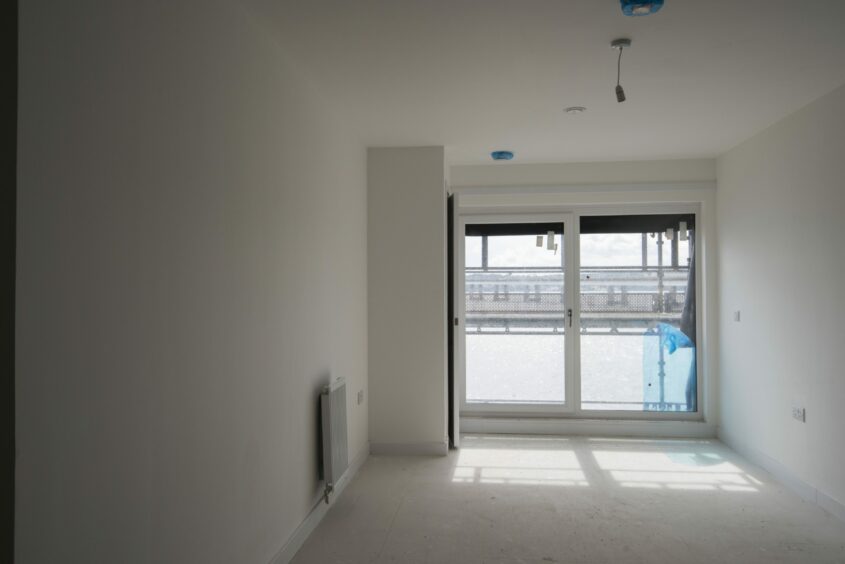 A main living space still under construction in one of the flats with sliding glass doors out to a balcony overlooking the river. 