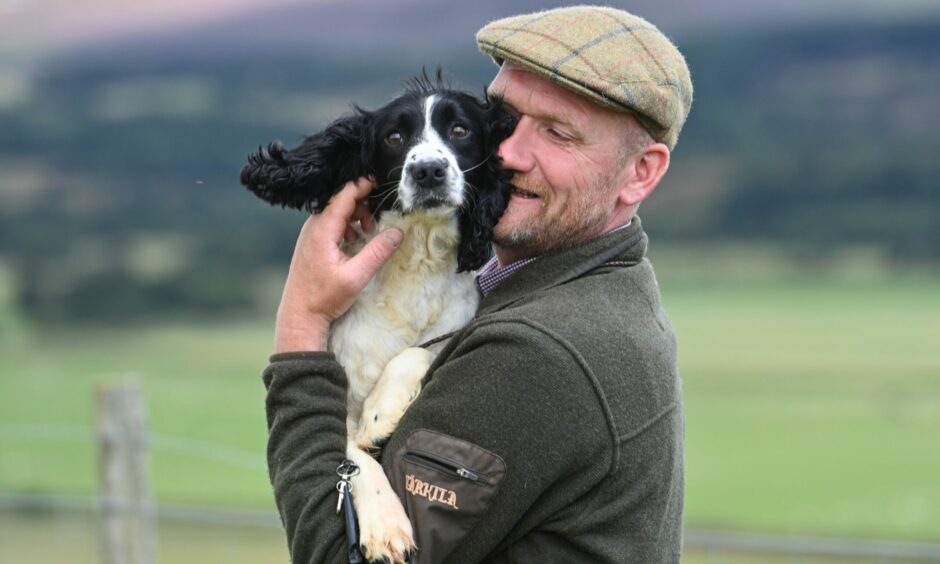 Photo shows a man in a tweet cap holding a black and white spaniel.