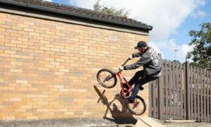 Courier News - Dundee - Kate Brown story - CR0037338 - John Buultjens is recreating his BMX stunt from the 90s on Monifieth High Street; on a wall near the Tesco. Picture Shows;  John Buultjens climbs the wall on his BMX bike, Union Street, Monifieth, 05th August 2022, Kim Cessford / DCT Media.