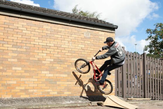 Courier News - Dundee - Kate Brown story - CR0037338 - John Buultjens is recreating his BMX stunt from the 90s on Monifieth High Street; on a wall near the Tesco. Picture Shows;  John Buultjens climbs the wall on his BMX bike, Union Street, Monifieth, 05th August 2022, Kim Cessford / DCT Media.