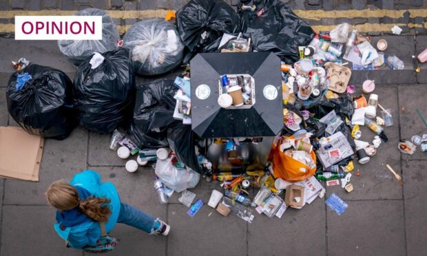 A member of the public walks past a bin overflowing with litter in Victoria Street in Edinburgh city centre.