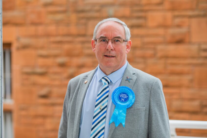 Councillor Chris Ahern in suit with blue Conservative Party rosette.