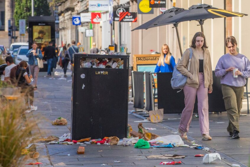 photo shows pedestrians walking past a bin overflowing with rubbish in Reform Street, Dundee.