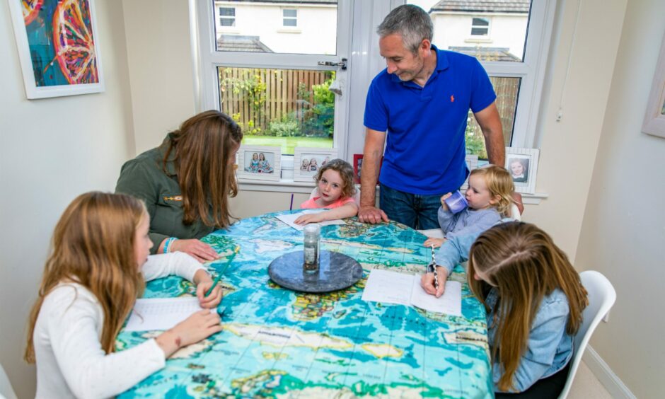 The Cunningham family, mum, dad and four girls gathered around the table for home school lessons