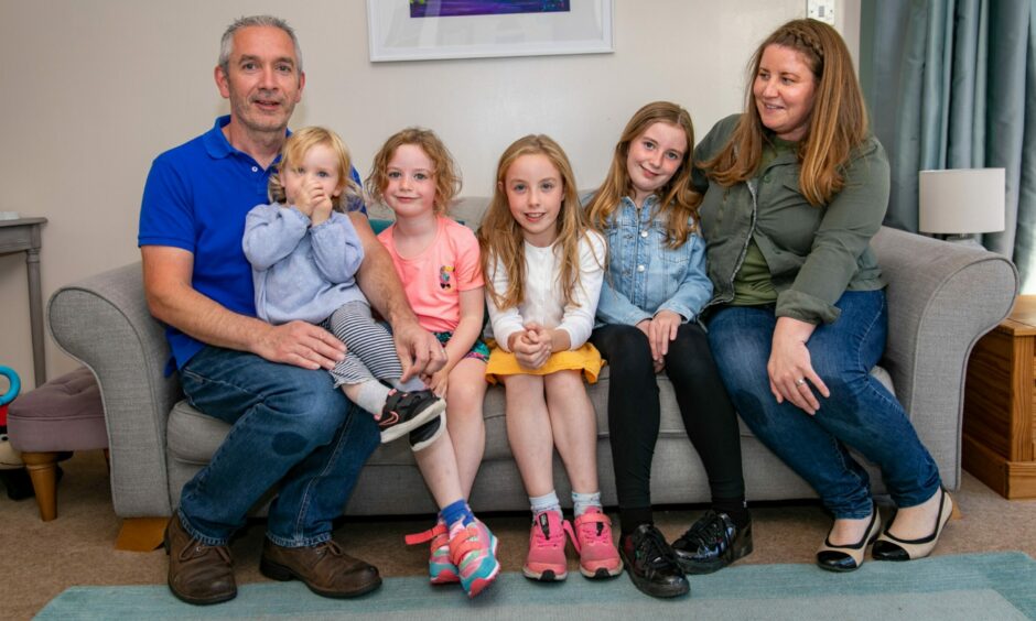 Parents Andrew and Kat sitting on the sofa with their four children Grace, Kate, Holly and Livia.
